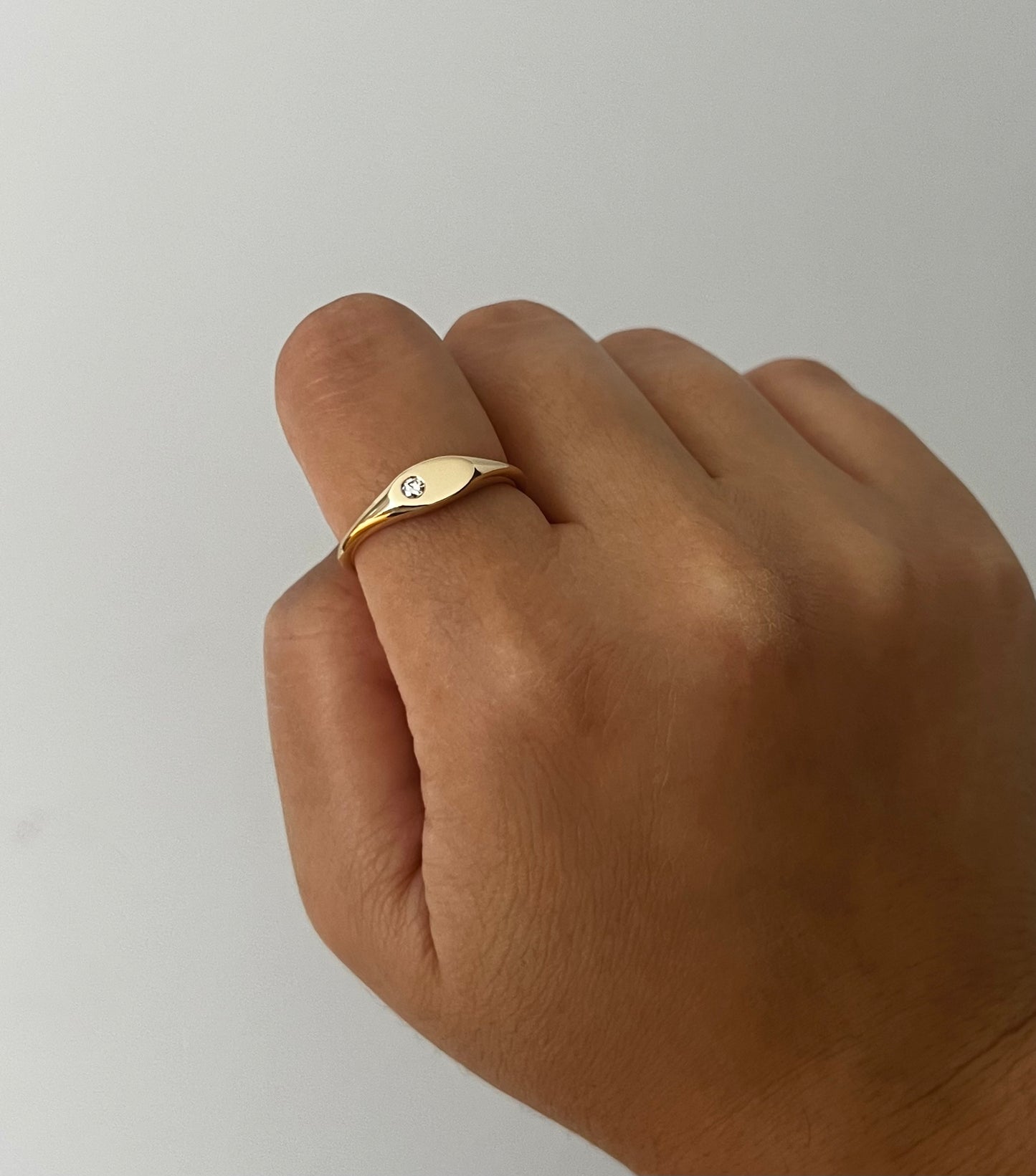 Gold ring with a diamond on a finger against a plain background